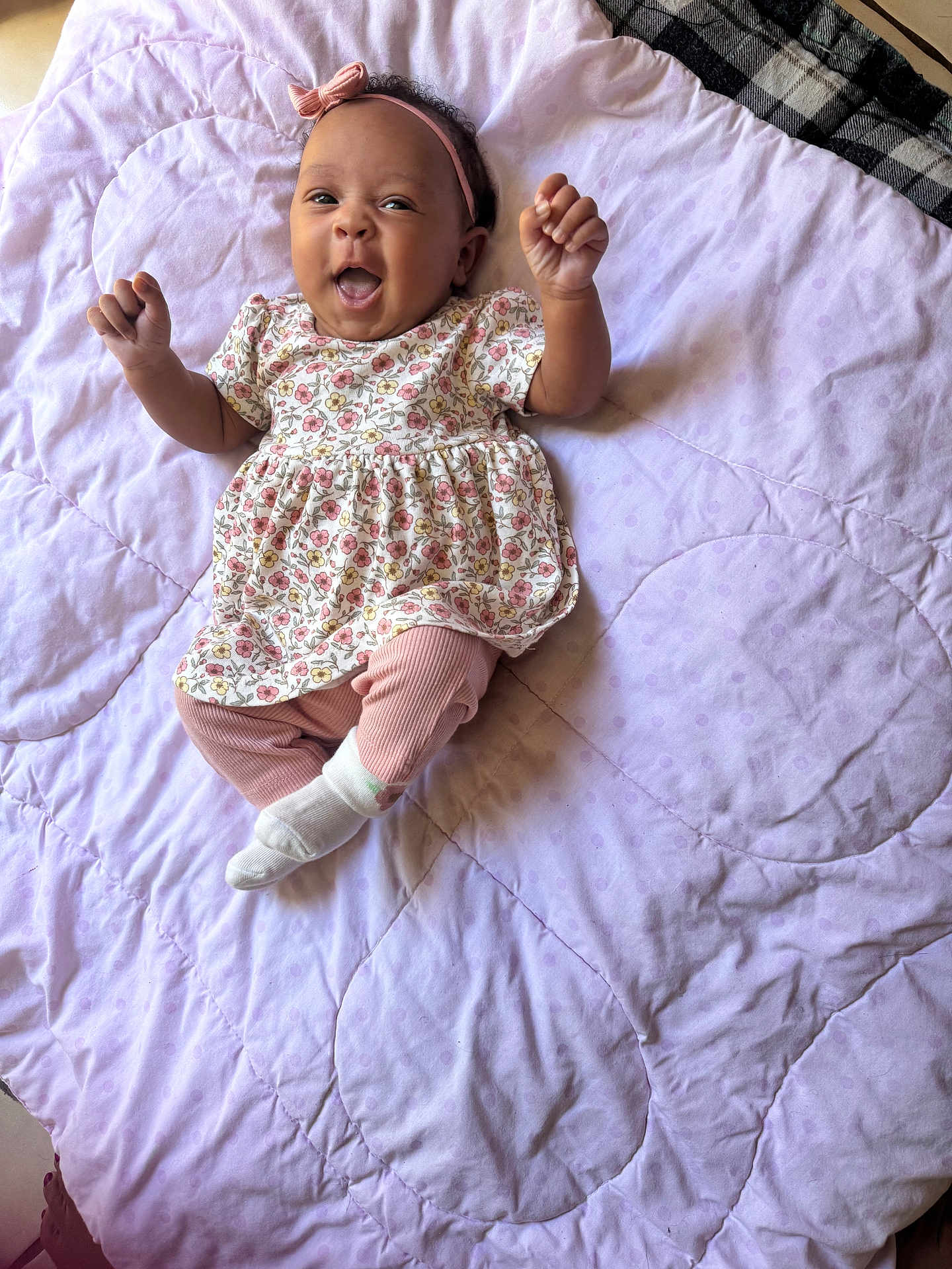Blakely joined the competition — help win amazing prizes! baby, child, infant, smiling, happy, lying_down, blanket, quilt, floral_dress, pink_leggings, headband, indoors, cute, raised_hands, expressive_face, soft_lighting, fabric, pattern, person, toddler