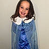 Aria is registered to the contest to win money with this photo: blue_dress, cape, celebration, child, costume, cute, face, fashion, girl, happy, indoor, long_hair, magic, person, portrait, princess_costume, smile, standing, wall, young