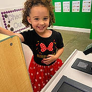 Aria joined the competition — help win amazing prizes! birthday_outfit, black_shirt, child, colorful_background, curly_hair, cute, educational_posters, girl, happy, indoor, learning_environment, person, play_area, play_checkout, polka_dots, preschool, red_skirt, retail_setup, smiling, toy_register