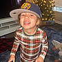 child, toddler, plaid, pajamas, cap, smiling, indoor, christmas_tree, lights, toy_story, carpet, living_room, furniture, window, curtains, footwear, happy, person, blur, motion