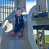 child, toddler, slide, playground, outdoor, smiling, curly_hair, nike, jacket, pants, red_shoes, blue_sky, grass, daylight, fun, playing, happy, person, leisure, recreation