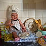 apron, baby, baking, bread, chef_hat, chocolate, cooking, countertop, eggs, flour, food, glass_bowl, infant, kitchen, kitchen_towel, oil_bottle, six_months, smiling, whisk, wooden_spoons