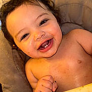 Xavier is registered to the contest to win money with this photo: baby, child, infant, smiling, happy, laughing, portrait, face, eyes, teeth, curly_hair, sitting, cushion, chair, indoor, warm_lighting, bare_chest, food, plate, closeup