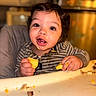 baby, child, crumbs, dining, eating, eyes, face, food, hair, hands, happy, high_chair, indoor, kitchen, portrait, sitting, smiling, striped_clothing, toddler, tray