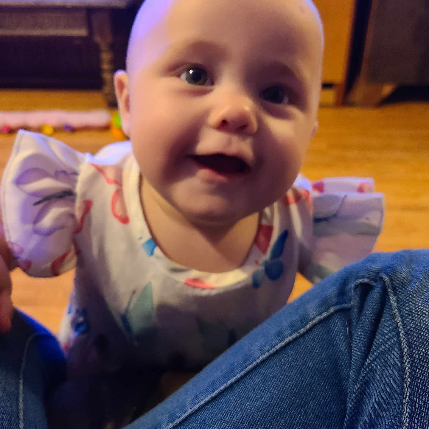 Lenore is registered to the contest to win money with this photo: baby, blurred_background, child, clothing, colorful, curious, cute, denim, face, happy, indoor, infant, joyful, knees, person, room, sitting, smiling, wooden_floor, young