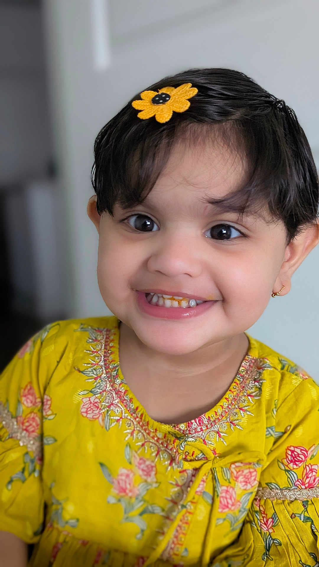 Nikki is registered to the contest to win money with this photo: child, toddler, smiling, face, flower_clip, yellow_dress, floral_pattern, earrings, portrait, indoors, happy, cute, young_child, black_hair, big_eyes, closeup, person, fashion, childhood, joy