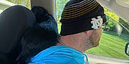 Butch joined the competition — help win amazing prizes! man, dog, car_interior, beanie, hoodie, driving, seat, window, daylight, black_dog, glasses, chain_necklace, headrest, greenery_outside, casual_clothing, side_view, pet, companion, relaxed, road_trip
