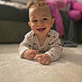 baby, smiling, carpet, floor, pajamas, child, indoor, person, happy, couch, blurred_background, home, cozy, infant, face, clothing, furniture, relaxing, cute, portrait