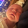 baby, sleeping, closeup, face, infant, peaceful, soft_lighting, cozy, white_garment, portrait, newborn, skin, head, mouth, nose, eyes_closed, indoor, blurred_background, rest, calm