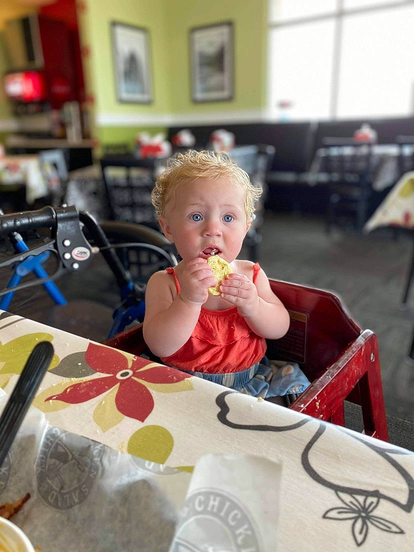 Kouvr is registered to the contest to win money with this photo: baby, baby_toddler_clothing, chair, child, cooking, dress, event, food, fun, kitchen_utensil, person, picture_frame, plate, room, sitting, spoon, surprise, sweetness, table, tableware