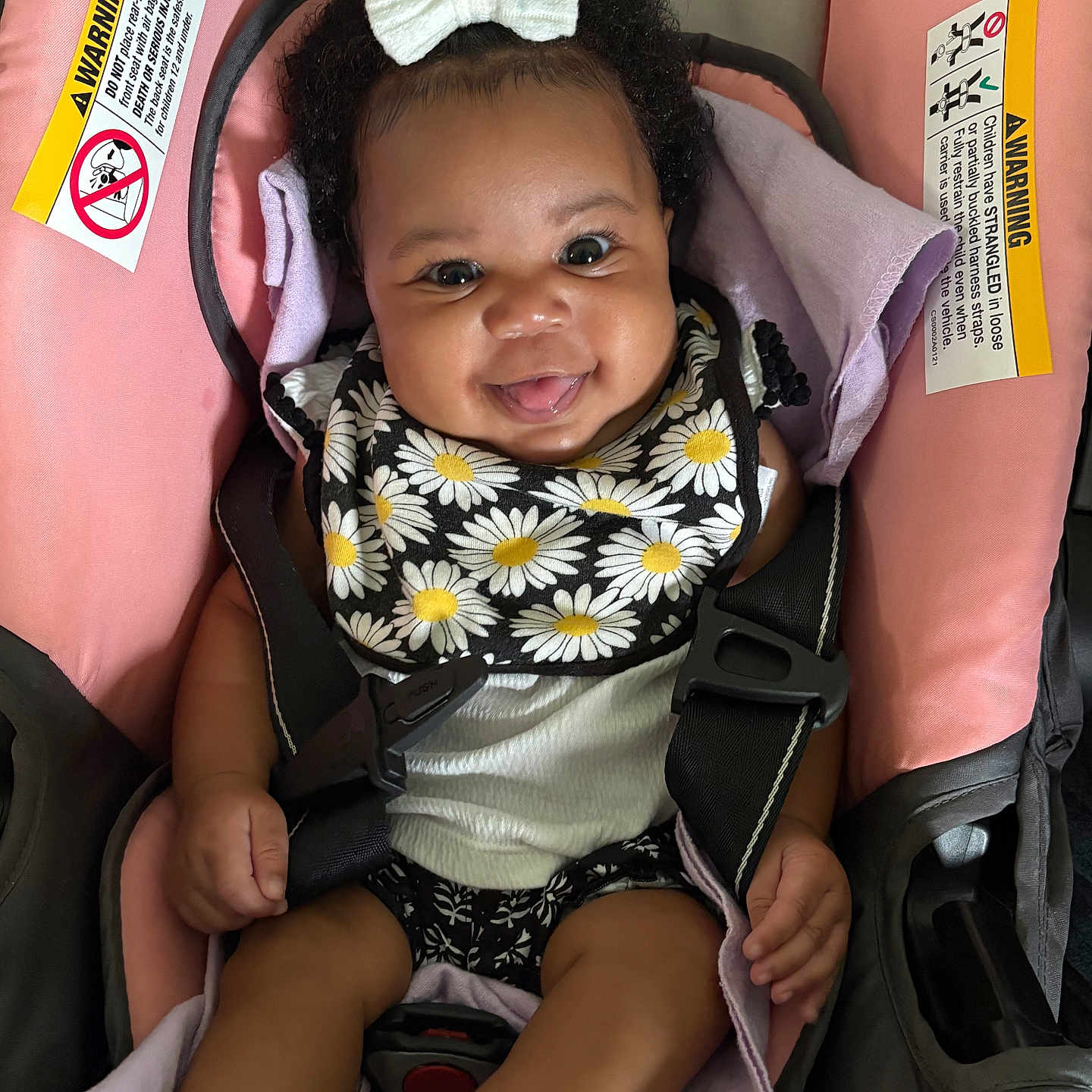 Kailyn is registered to the contest to win money with this photo: baby, bib, black_clothing, bow, car_seat, child, curly_hair, cute, daisy_pattern, happy, indoor, infant, person, pink, playful, portrait, seatbelt, smiling, toddler, white_socks