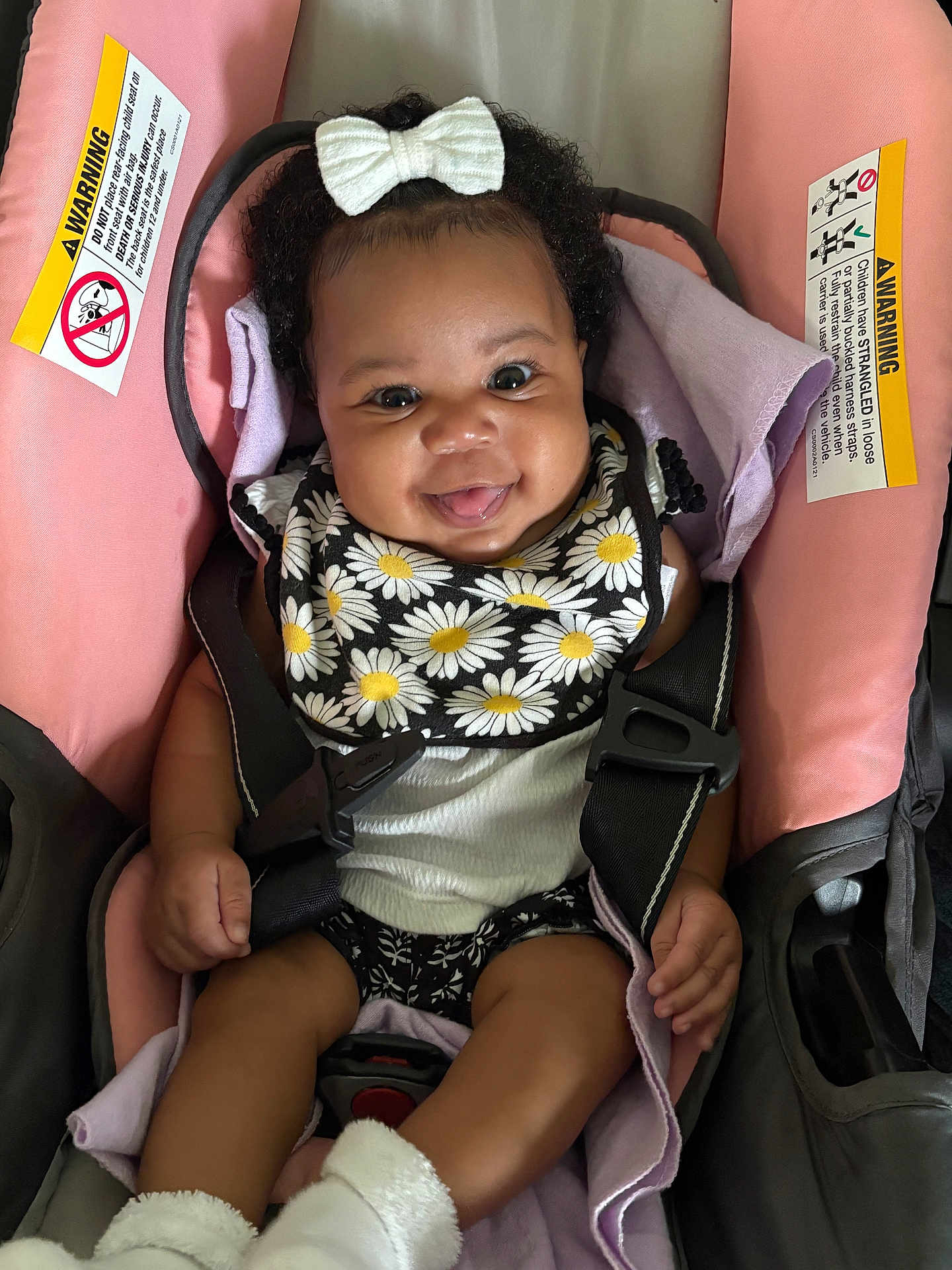 Kailyn is registered to the contest to win money with this photo: baby, smiling, car_seat, bow, curly_hair, bib, daisy_pattern, white_socks, infant, cute, happy, child, seatbelt, pink, black_clothing, person, indoor, portrait, toddler, playful