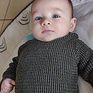 Kenneth a rejoint le concours — aidez-le/la à gagner de superbes lots ! baby, child, infant, face, eyes, sweater, knitwear, hand, portrait, closeup, lying_down, indoor, soft_surface, patterned_background, cute, young_child, skin, head, expression, person