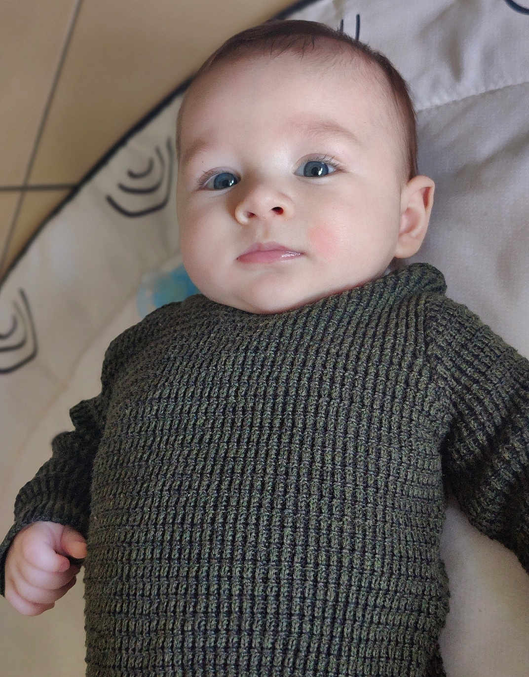 Kenneth a rejoint le concours — aidez-le/la à gagner de superbes lots ! baby, child, infant, face, eyes, sweater, knitwear, hand, portrait, closeup, lying_down, indoor, soft_surface, patterned_background, cute, young_child, skin, head, expression, person