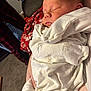 Jorah is registered to the contest to win money with this photo: baby, newborn, sleeping, blanket, white_clothing, animal_print, indoor, person, hand, plaid_pajamas, red_blanket, carpet, cozy, peaceful, face, infant, wrapped, resting, comfort, soft