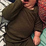 baby, infant, child, face, hand, clothing, ribbed_fabric, bed, blanket, pillow, curious, lying_down, indoors, cute, skin, expression, wide_eyes, cozy, comfortable, young