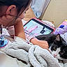child, cat, tablet, blanket, bed, indoor, relaxed, cuddling, black_and_white_cat, soft_texture, casual_clothing, technology, curtain, toy, resting, close_up, pet, comfort, sleepwear, home