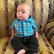 Samuel is registered to the contest to win money with this photo: baby, child, plaid_shirt, blue_shirt, black_pants, barefoot, couch, upholstery, patterned_fabric, indoor, sitting, portrait, infant, curious, person, young_child, face, head, expression, home
