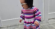 Abigail joined the competition — help win amazing prizes! toddler, child, dress, striped_clothing, sneakers, outdoor, paved_ground, white_fence, braided_hair, hair_bow, sunglasses, side_view, walking, cute, young_child, fashion, daylight, person, colorful, playful