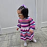 toddler, child, dress, striped_clothing, sneakers, outdoor, paved_ground, white_fence, braided_hair, hair_bow, sunglasses, side_view, walking, cute, young_child, fashion, daylight, person, colorful, playful