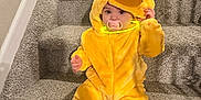 Elleigh is registered to the contest to win money with this photo: toddler, child, costume, duck, yellow, stairs, carpet, pacifier, glow_necklace, cute, indoor, sitting, plush, clothing, baby, face, sock, hand, expression, portrait