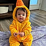 baby, child, costume, duck, yellow, blanket, purple, indoor, floor, pacifier, cute, sitting, face, hood, plush, person, feet, wood_floor, furniture, door