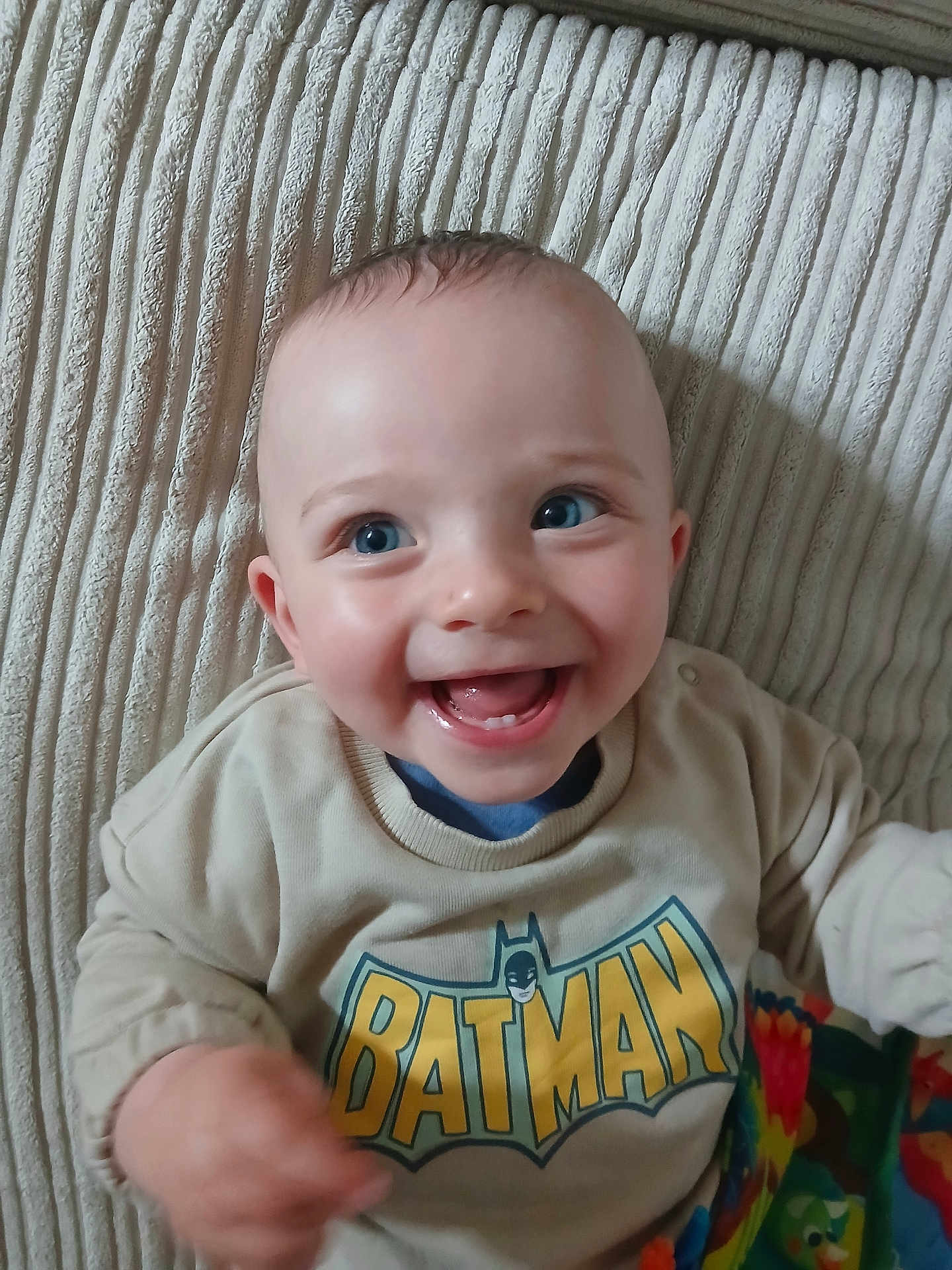 Ruben joined the competition — help win amazing prizes! baby, child, smiling, batman_sweatshirt, blue_eyes, teeth, happy, person, clothing, blanket, texture, indoors, cute, infant, portrait, sitting, casual_wear, young_child, joyful, bright