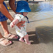 Ruben joined the competition — help win amazing prizes! baby, child, adult, water, beach, sand, blue_hat, romper, barefoot, summer, sunny, outdoor, nature, playing, water_sport, people, trees, footwear, hand, shore