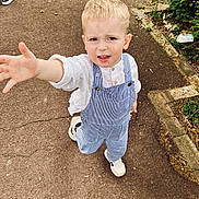 Stefan participe au concours pour gagner de l'argent avec cette photo : blond_hair, boy, casual_clothing, child, curious, daylight, expression, greenery, nature, outdoor, overalls, pavement, person, plant, reaching_hand, sidewalk, sneakers, walking, white_shirt, young