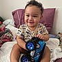 baby, child, toy, blue_toy, truck, bed, blanket, pillow, smile, happy, indoors, clothing, cute, feet, hand, face, curly_hair, infant, playful, person