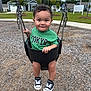 toddler, child, swing, playground, green_shirt, sneakers, curly_hair, smiling, park, suburban, trees, grass, sidewalk, daytime, outdoor, person, happy, fun, play, baby