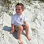 child, boy, sand, beach, barefoot, grass, smile, white_tshirt, shorts, necklace, sunlight, outdoor, nature, happy, sitting, summer, casual_clothing, portrait, daylight, vacation