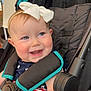 baby, child, smile, face, headband, bow, stroller, seatbelt, blue_eyes, red_cheeks, clothing, patterned_clothes, happy, infant, person, indoor, black_stroller, teal_trim, cute, portrait