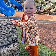 Gentry is registered to the contest to win money with this photo: toddler, child, playground, slide, blue_slide, outdoor, smiling, fall_clothing, pumpkin_pattern, toy_log, grass, sunny, daytime, play_area, person, happy, cute, ruffled_pants, park, recreation
