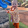 toddler, child, playground, slide, blue_slide, outdoor, smiling, fall_clothing, pumpkin_pattern, toy_log, grass, sunny, daytime, play_area, person, happy, cute, ruffled_pants, park, recreation