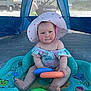 baby, child, inflatable_pool, sun_hat, swimsuit, plastic_toys, beach, canopy, outdoor, summer, water_toy, tent, shade, person, sand, building, window, toy_rings, cute, play