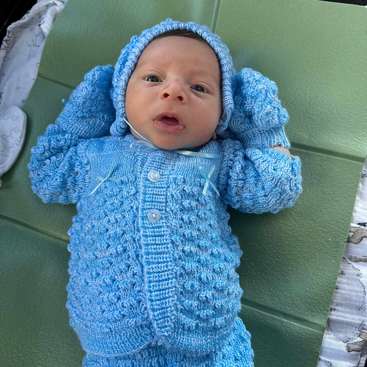 Victor Valentino joined the competition — help win amazing prizes! baby, blue_knitwear, child, cozy, cute, eyes_open, face, green_mat, hands_up, indoor, infant, knit_hat, knit_mittens, knit_pants, knit_sweater, lying_down, newborn, portrait, small_person, soft_texture