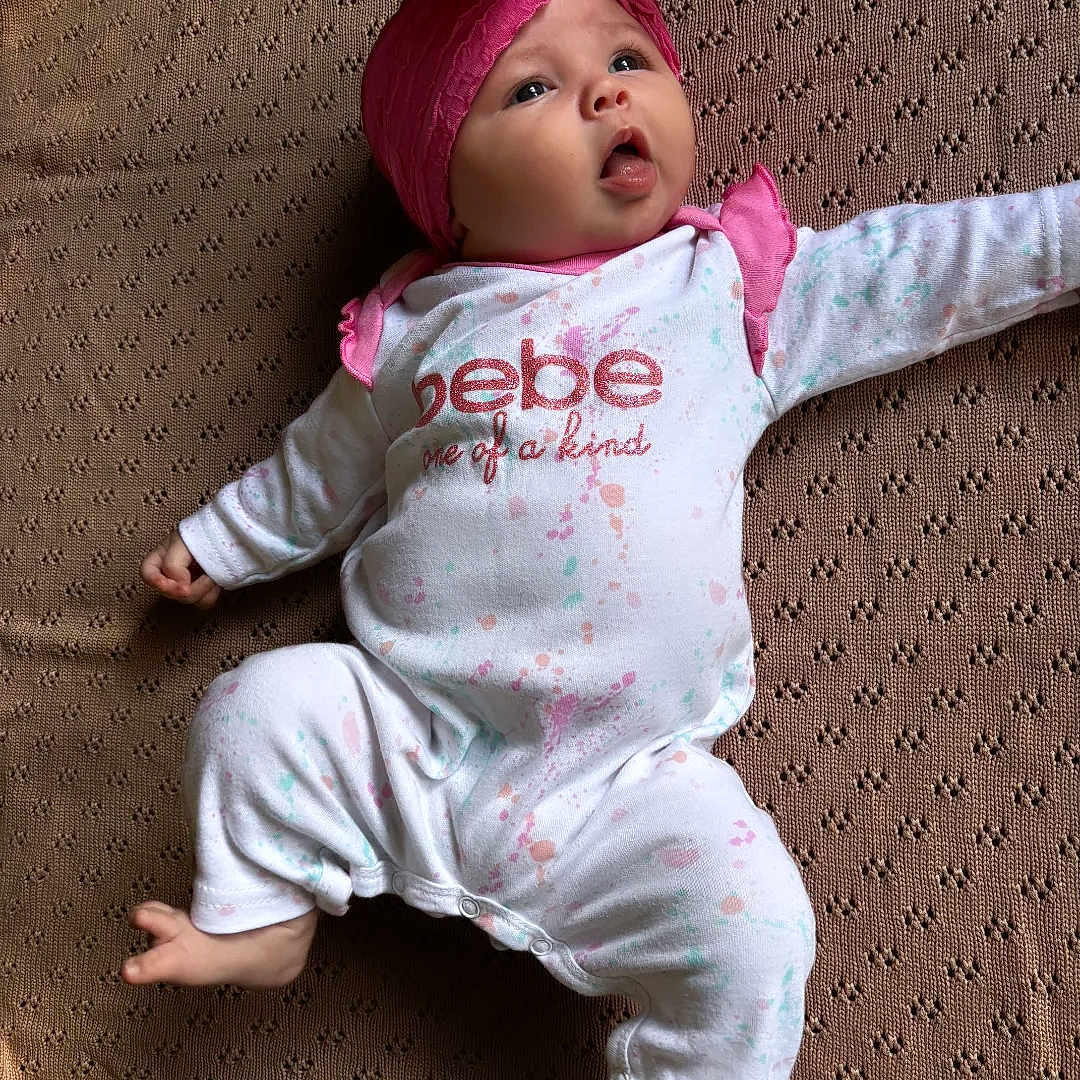 Delaney is registered to the contest to win money with this photo: baby, blanket, child, clothing, cute, expression, headband, home, indoors, infant, looking_up, lying_down, onesie, peaceful, pink, portrait, small_feet, small_hands, soft_lighting, texture
