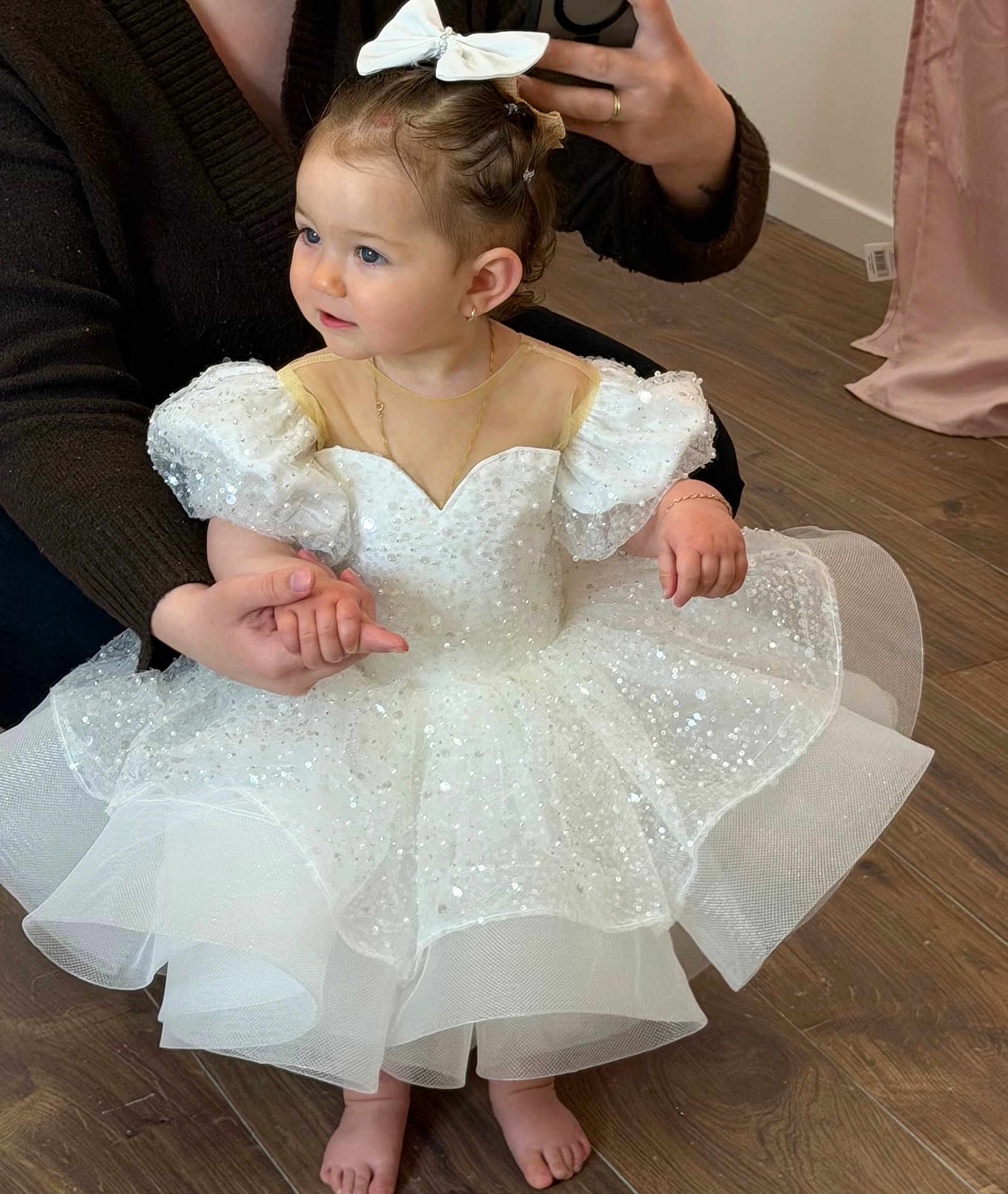 Mia.r participe au concours pour gagner de l'argent avec cette photo : child, toddler, little_girl, white_dress, tulle, sequins, bow, hair_bow, sparkle, barefeet, sitting, holding_hands, adult_hand, necklace, bracelet, earrings, wood_floor, boutique, portrait, cute