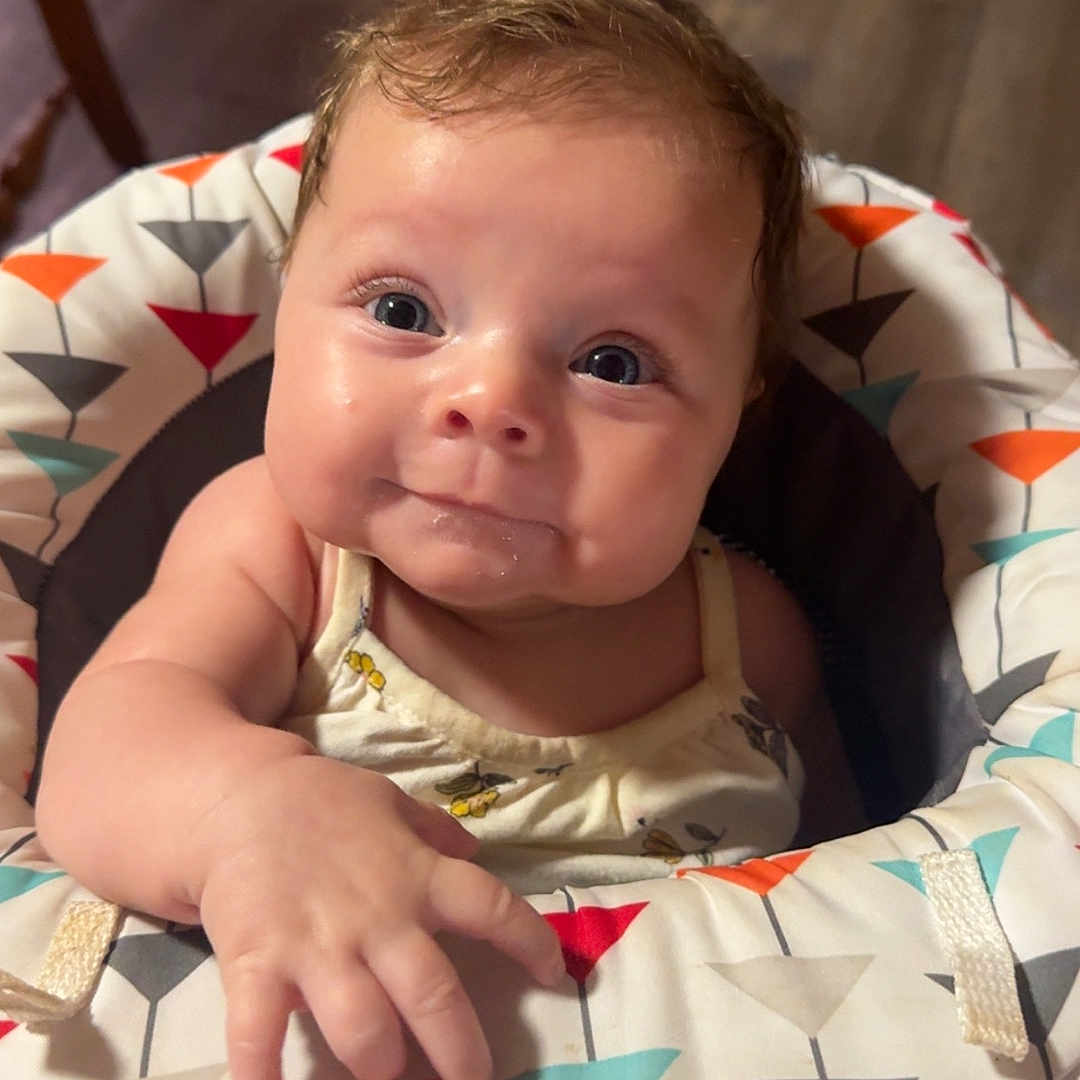 Rylin is registered to the contest to win money with this photo: baby, child, closeup, clothing, curious, cute, expression, eyes, face, floor, hand, happy, indoor, infant, patterned, person, seat, smiling, wooden_floor, young