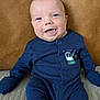 baby, smiling, onesie, blue_clothing, infant, cute, portrait, sitting, happy, face, child, indoor, leather_background, soft_surface, young_child, eyewear_absent, short_hair, buttoned_clothing, closeup, human