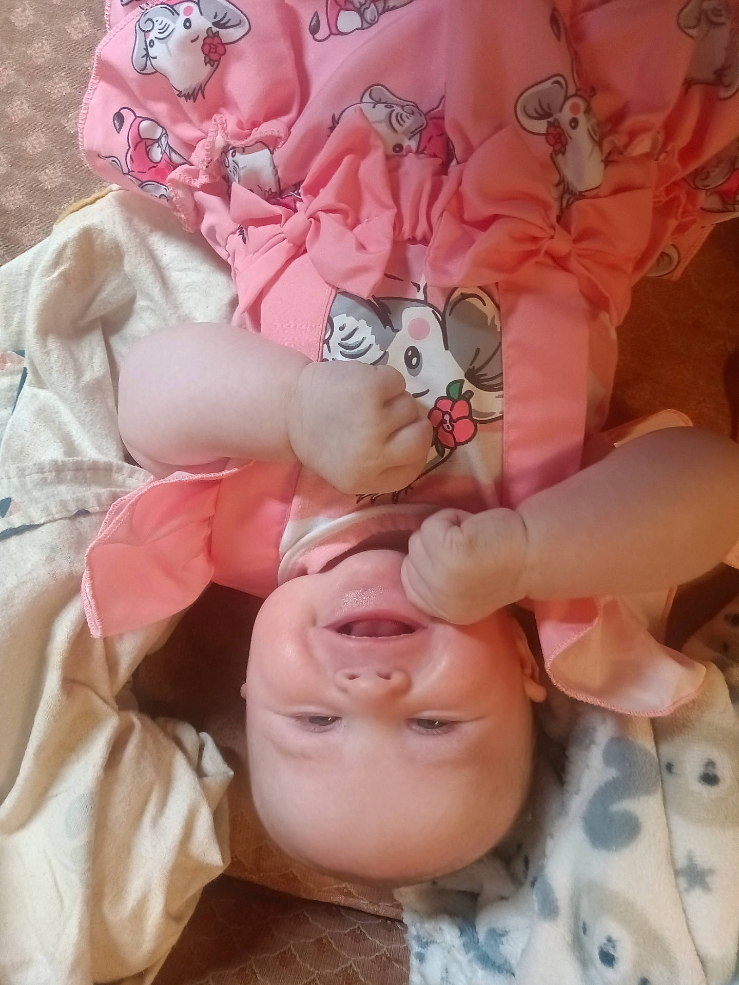 baby, blanket, child, chubby_cheeks, closeup, cozy, cute, face, fist, happy, indoors, infant, lying_down, mouse_print, pink_clothing, skin, sleepwear, smiling, soft_fabric, toddler