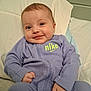 baby, child, clothing, cozy, cute, eyes, face, hands, happy, head, indoor, infant, nike_logo, person, pillow, portrait, purple_onesie, sitting, smiling, young