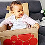 toddler, child, cardboard_box, couch, smiling, curly_hair, indoor, white_clothing, pink_sweater, happy, sitting, home, playful, furniture, person, portrait, baby, cozy, relaxing, cute