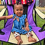 toddler, child, outdoor, chair, blue_dress, polka_dot_bow, cow_print_leggings, grass, blanket, purple_chair, smiling, barefoot, curly_hair, bracelet, earrings, sunny_day, park, playful, happy, person