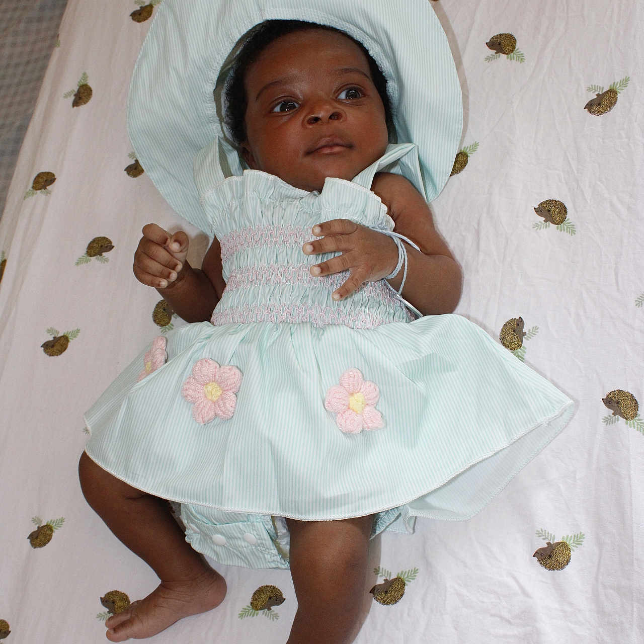Adira is registered to the contest to win money with this photo: adorable, baby, bonnet, child, clothing, cute, dress, fabric, feet, flower, hands, hedgehog, indoor, infant, lying_down, pattern, portrait, sheet, skin, young