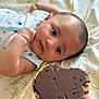 baby, infant, face, hand, chocolate, biscuit, food, blanket, bed, curious, lying_down, person, skin, expression, closeup, focus, comfort, indoor, soft_lighting, nourishment
