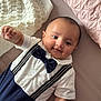 Ibrahim is registered to the contest to win money with this photo: baby, infant, smiling, bow_tie, suspenders, white_shirt, navy_pants, bed, blanket, pillow, cute, portrait, child, person, indoors, soft_lighting, happy, lying_down, closeup, young
