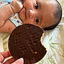 Ibrahim is registered to the contest to win money with this photo: baby, infant, face, hand, chocolate, biscuit, food, bed, blanket, pattern, skin, person, lying_down, closeup, fingers, snack, cute, eyes, focus, curious