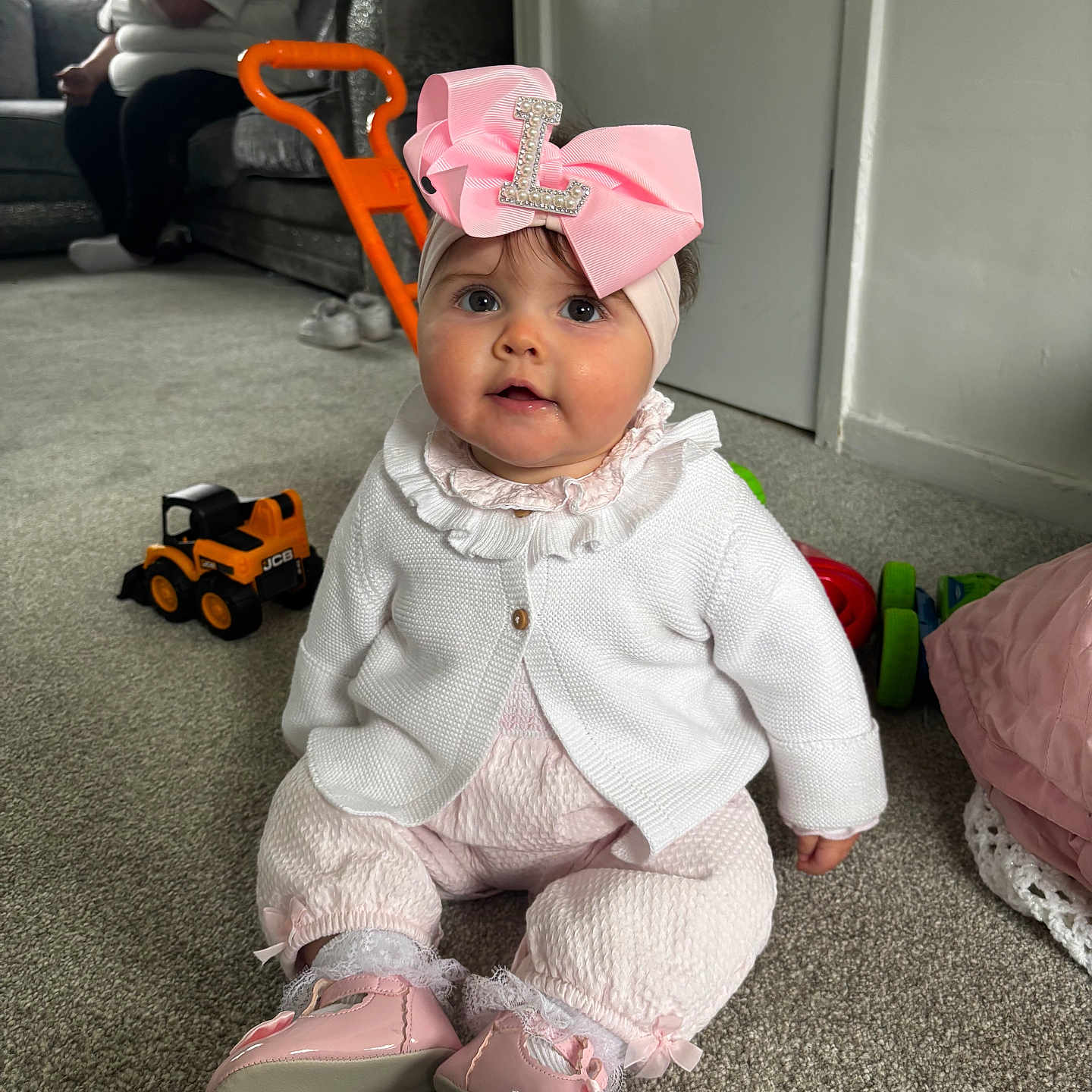 Lilah is registered to the contest to win money with this photo: baby, child, indoor, carpet, toy, pink_bow, headband, white_cardigan, pink_shoes, woman, sofa, phone, living_room, person, floor, window, casual, playful, home, cute